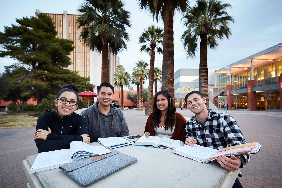 Four students sitting around a table outside studying.