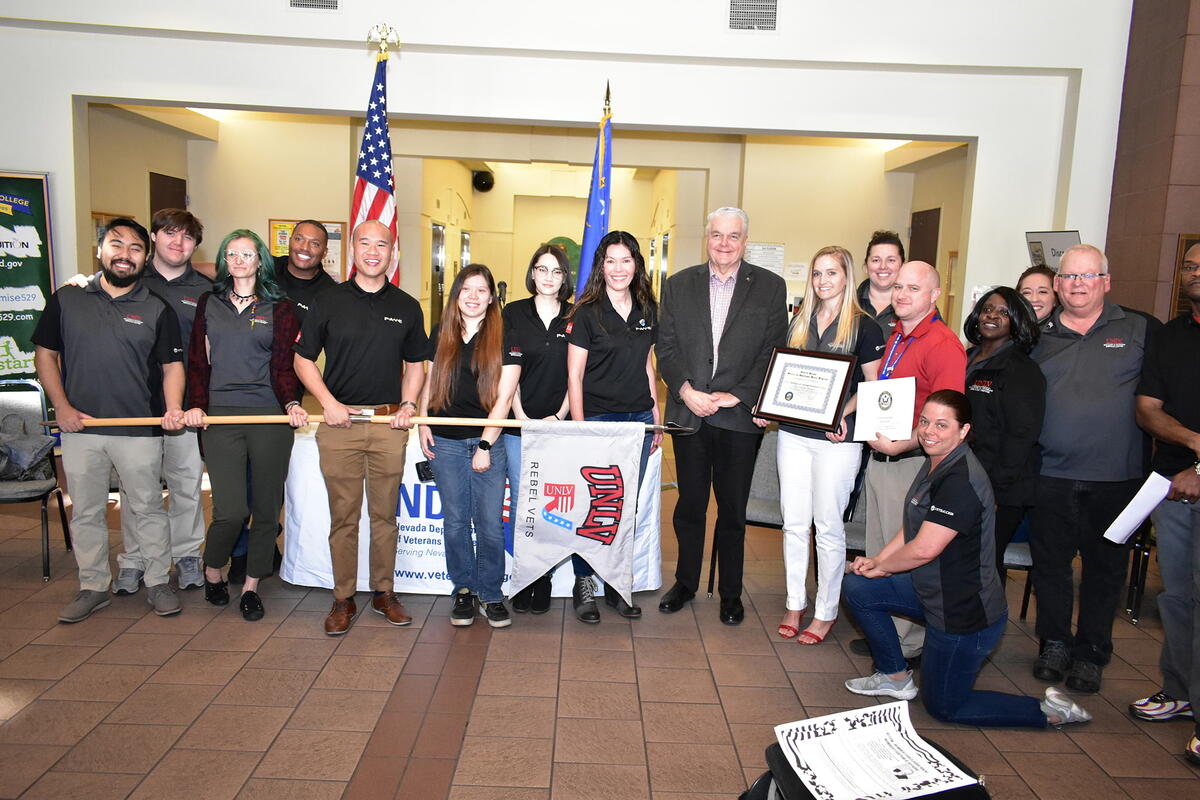 Group of people holding a Rebel Vets flag and framed certificates