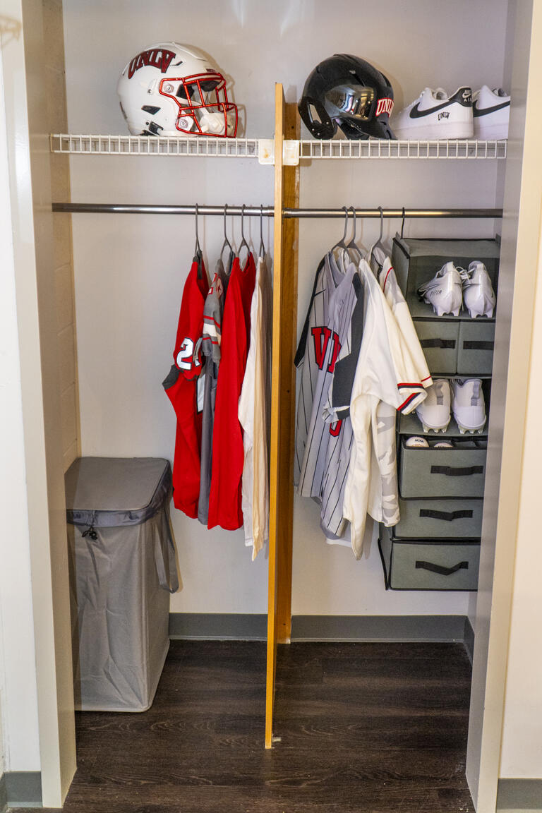 A look into a dorm closet, with a few shirts, shoes and hats inside