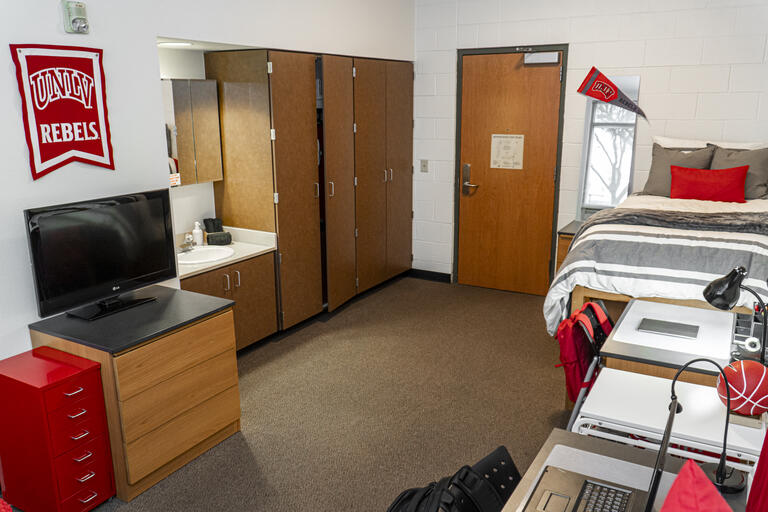 An overview of a single dorm room with TV, sink, shared bathroom, and two beds